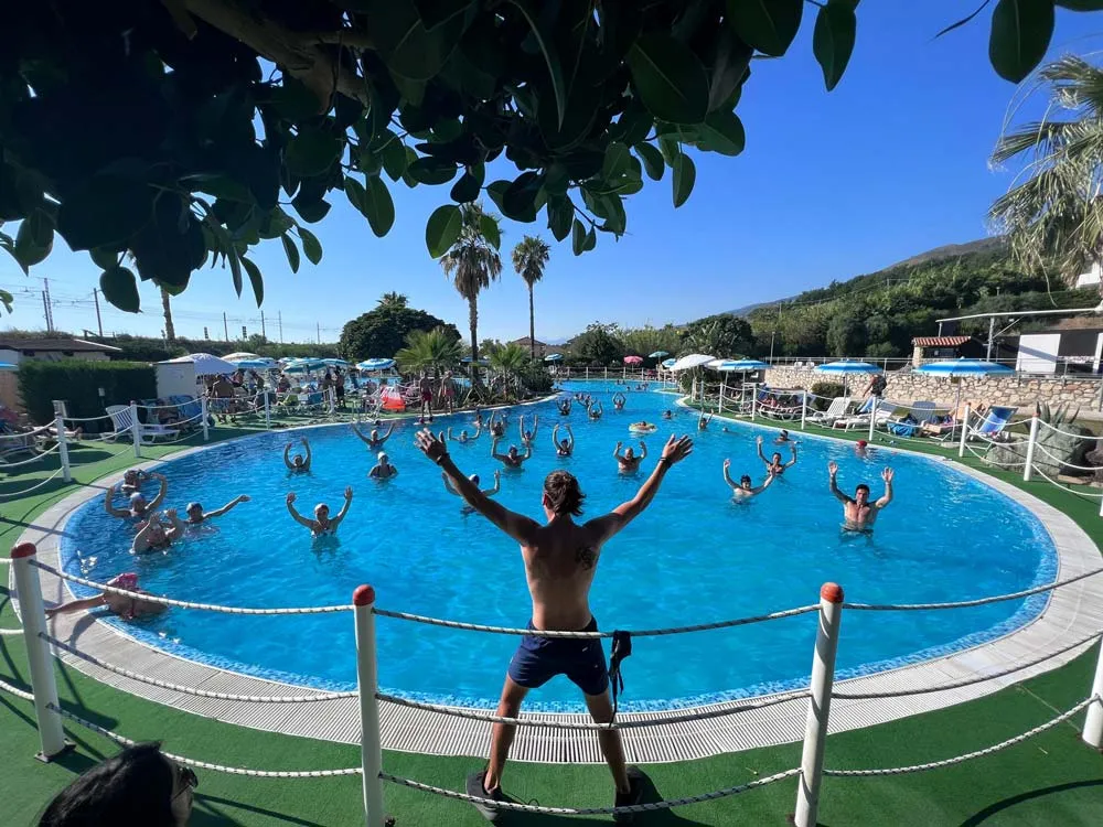 Animatore guida lezione di acquagym in piscina con ospiti e palme sullo sfondo