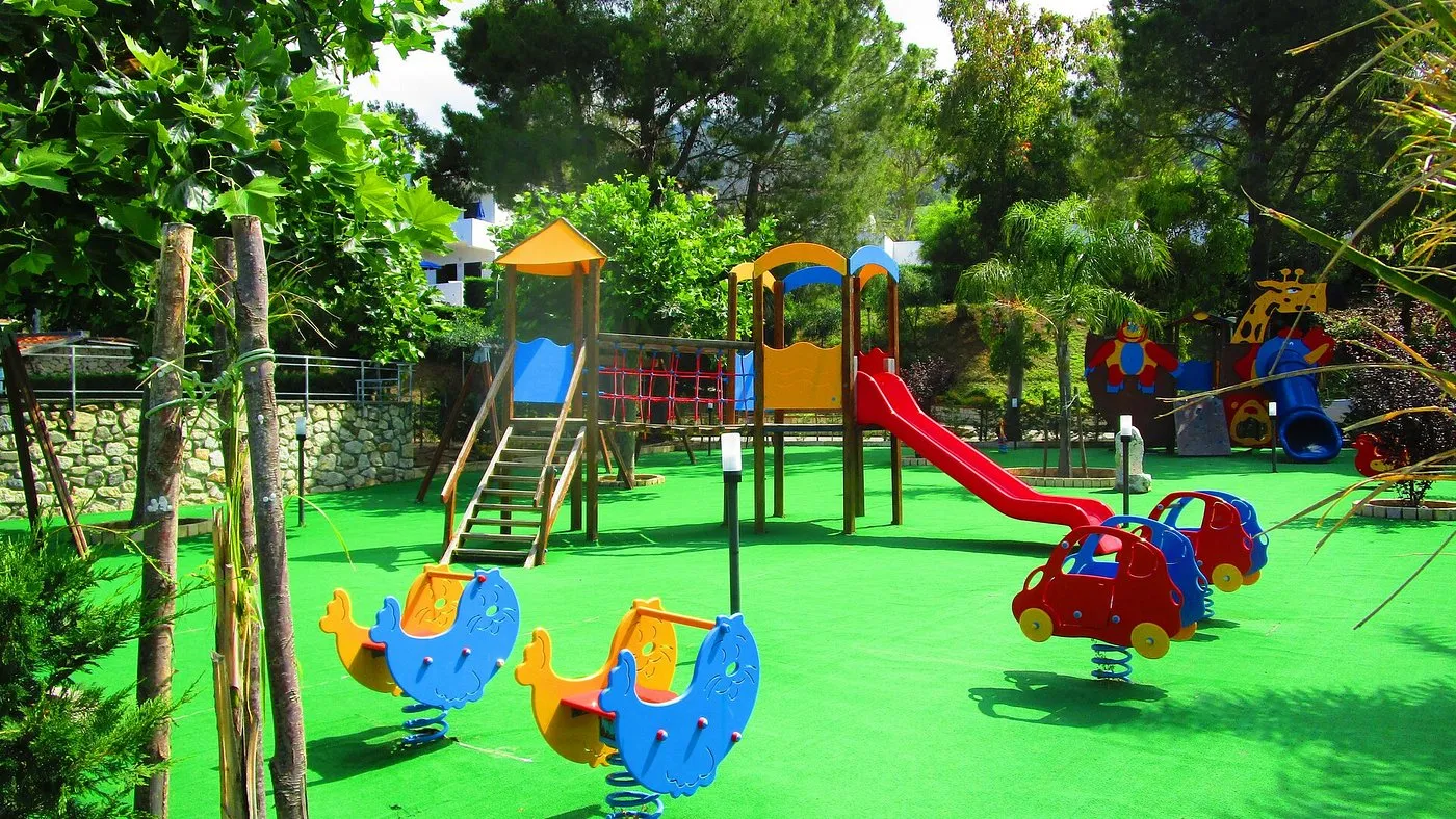 Area giochi per bambini con scivolo, giostre e prato verde tra gli alberi