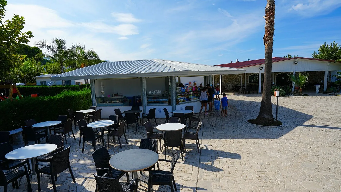 Bar esterno del resort con tavoli, sedie e palme sotto cielo sereno