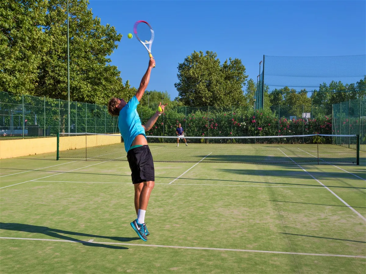 Giocatore di tennis in azione sul campo in erba sintetica del resort