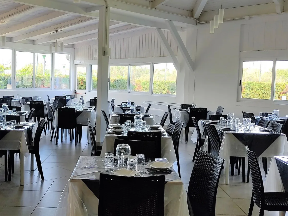 Sala ristorante luminosa con tavoli apparecchiati e grandi finestre