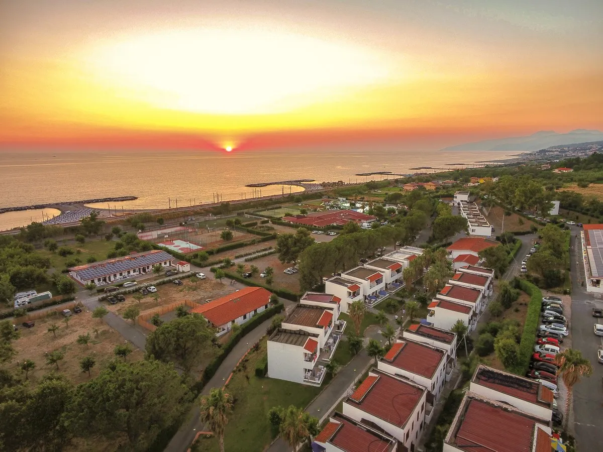 Tramonto sul mare con vista aerea del resort e delle villette dai tetti rossi
