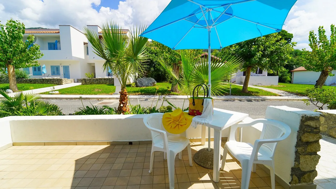Terrazza con tavolo, sedie bianche e ombrellone azzurro vista giardino