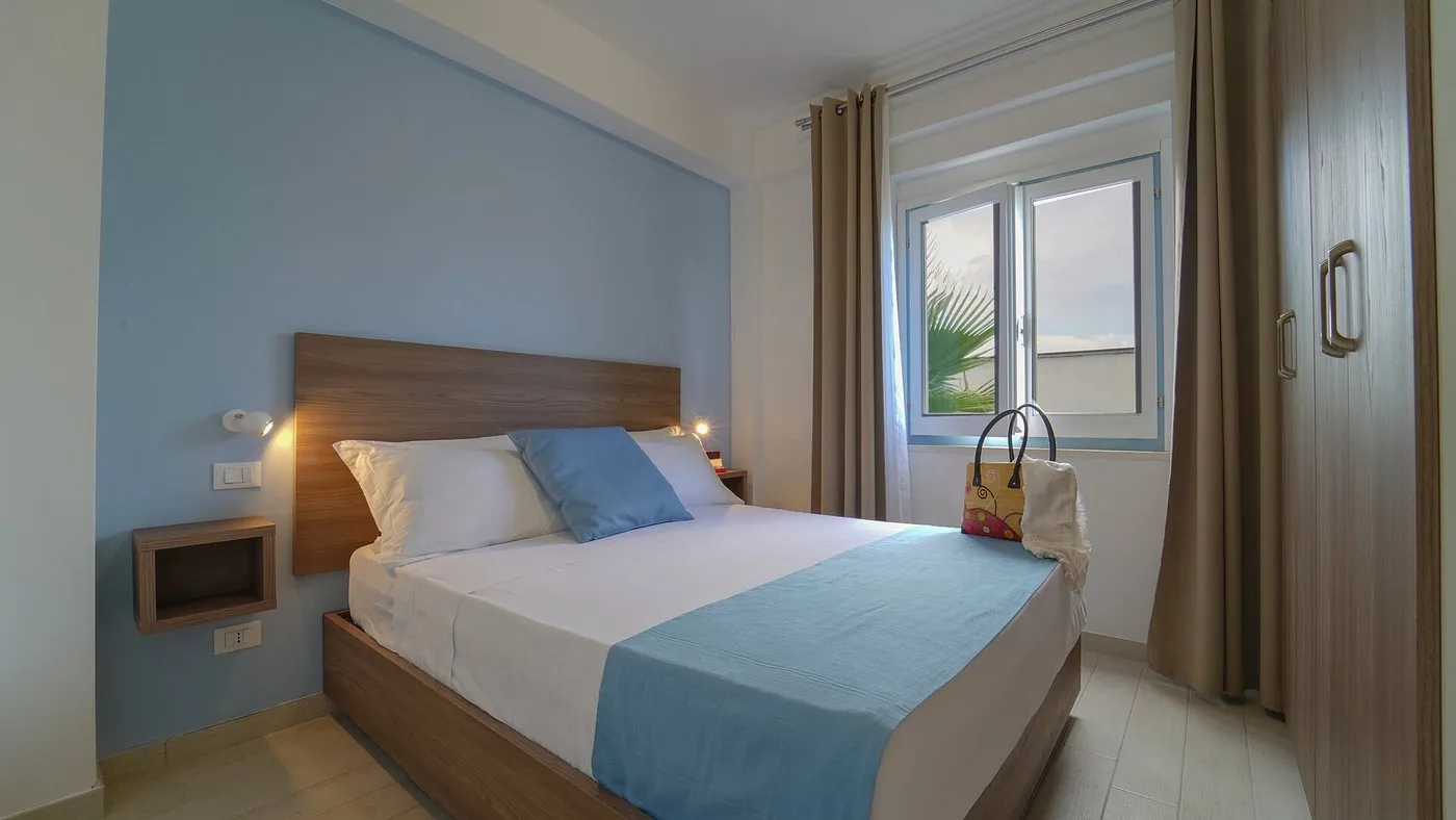 Camera da letto matrimoniale con parete azzurra, armadio in legno e finestra