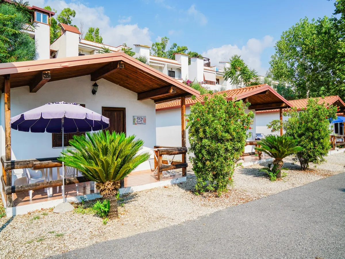 Bungalow bianchi con tettoie in legno, ombrelloni e vegetazione mediterranea
