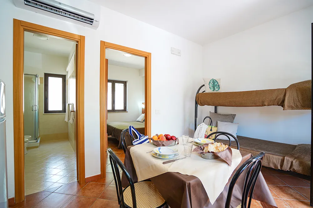 Soggiorno dell'appartamento con tavolo apparecchiato, letto a castello e cucina