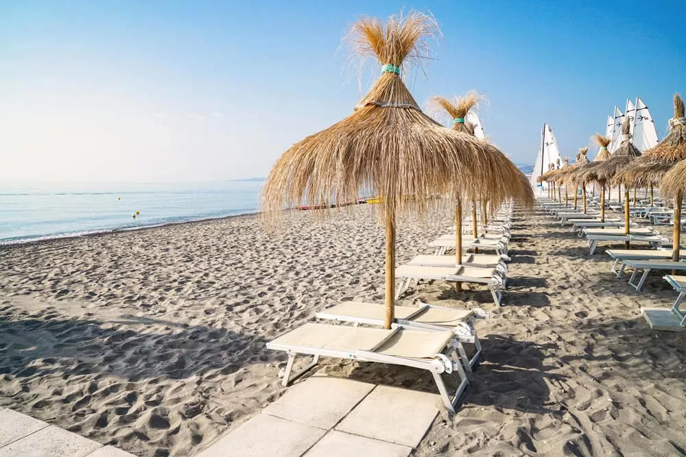 Ombrelloni in paglia e lettini allineati sulla spiaggia in riva al mare
