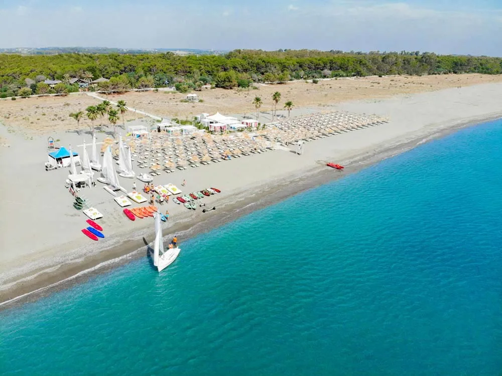 Spiaggia sabbiosa con ombrelloni in paglia e sport acquatici sul mare turchese