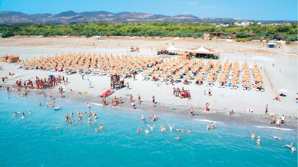 Spiaggia affollata con ombrelloni in paglia e bagnanti in acqua