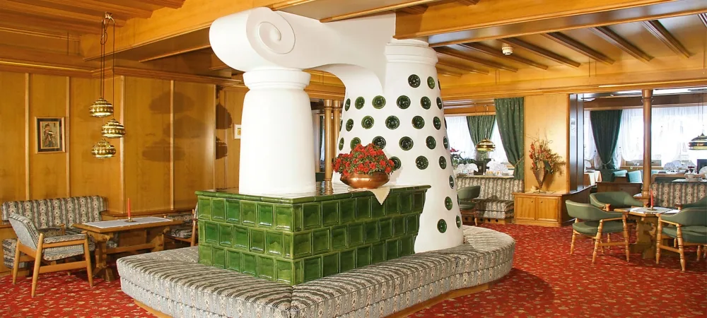 Hall dell'hotel con boiserie in legno, stufa in maiolica verde e poltrone