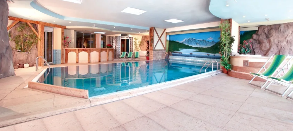 Piscina coperta con lettini, decorazioni rocciose e murale paesaggistico