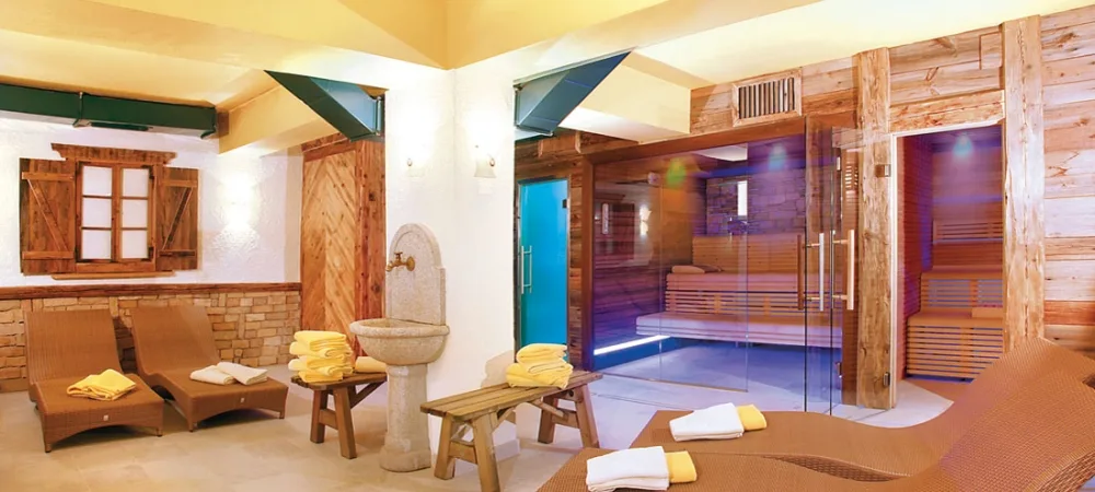 Area spa con sauna in legno, lettini relax e fontana in pietra