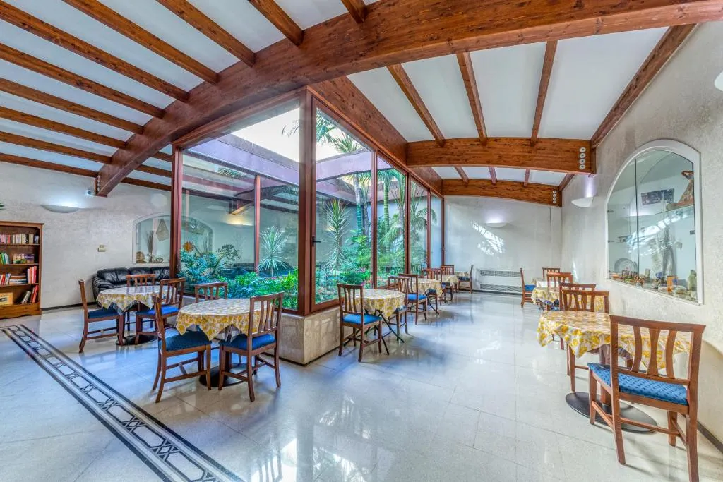 Sala ristorante luminosa con soffitto a travi in legno, tavoli apparecchiati e ampie vetrate sul giardino
