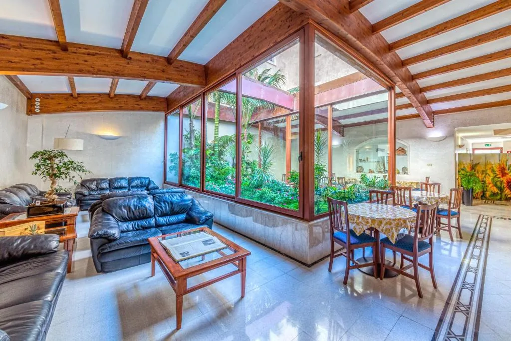 Hall con divani in pelle nera, tavolino e grandi vetrate affacciate su un giardino tropicale interno
