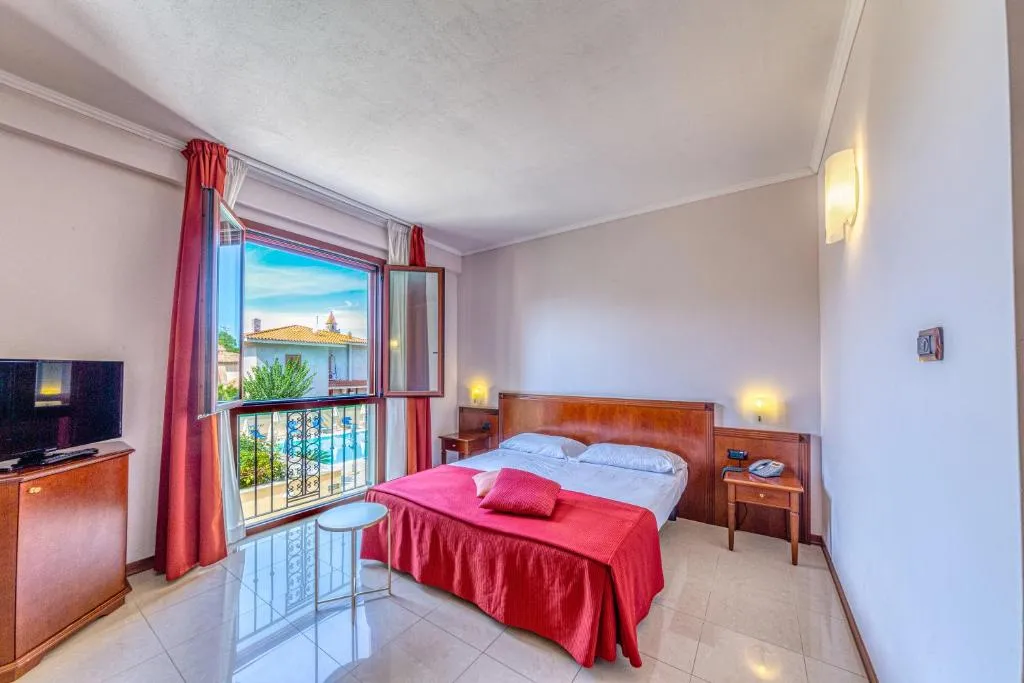 Camera matrimoniale con copriletto rosso, TV e finestra panoramica con vista sulla piscina