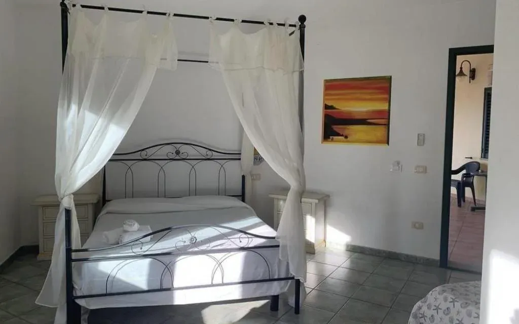 Camera da letto con letto a baldacchino in ferro battuto, tende bianche e quadro con tramonto