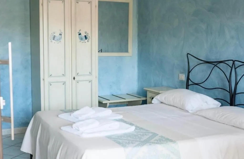 Camera da letto con pareti azzurre, letto matrimoniale, armadio decorato e asciugamani bianchi