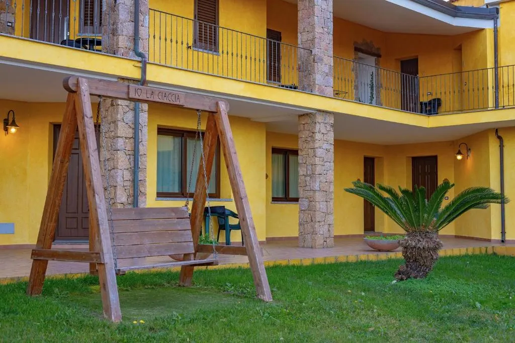 Esterno dell'hotel giallo con altalena in legno, colonne in pietra, balconi e giardino