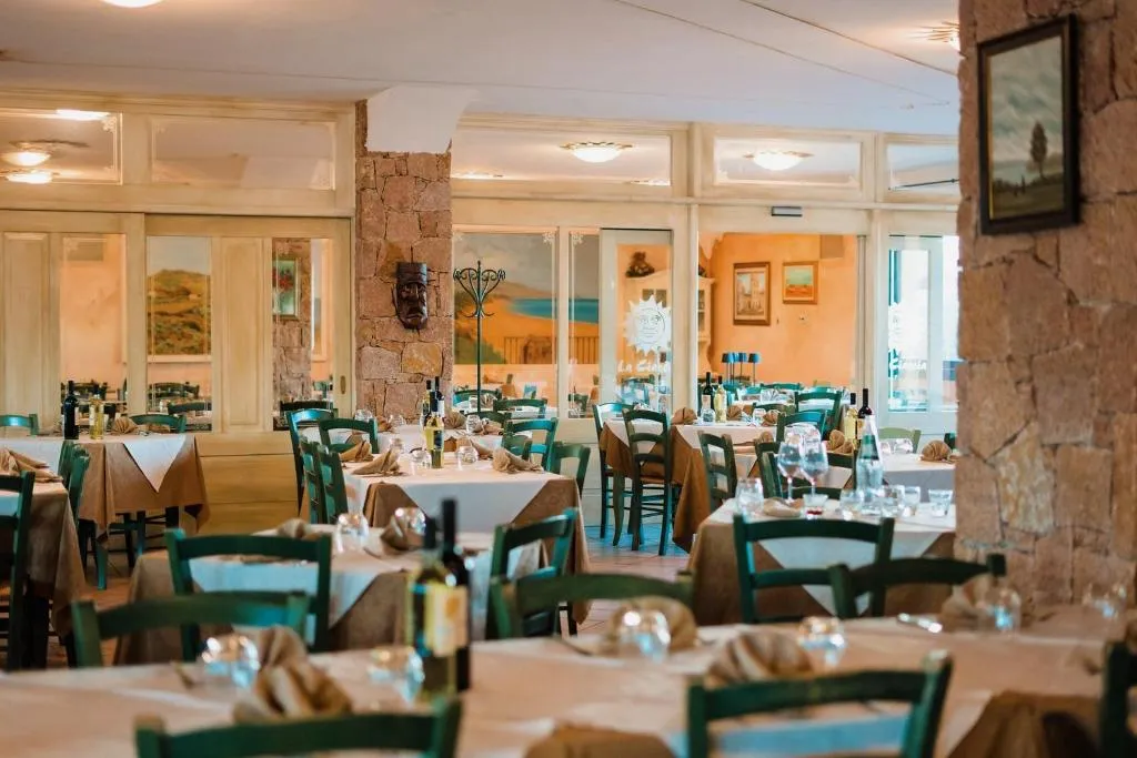 Sala ristorante interna con tavoli apparecchiati, sedie verdi, colonne in pietra e quadri alle pareti