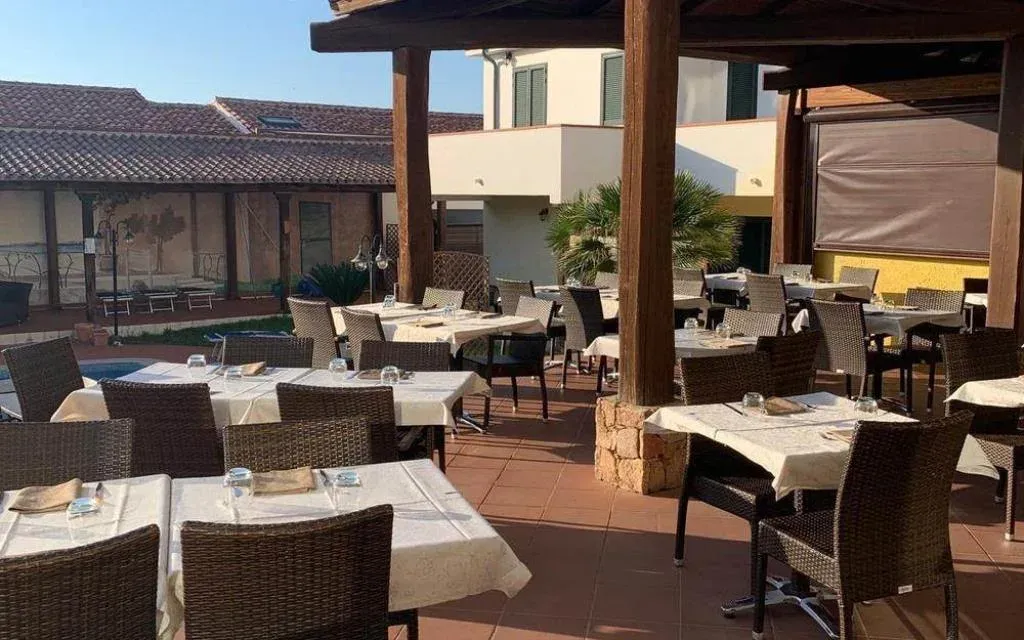 Ristorante all'aperto con tavoli apparecchiati, sedie in rattan e porticato in legno vicino alla piscina