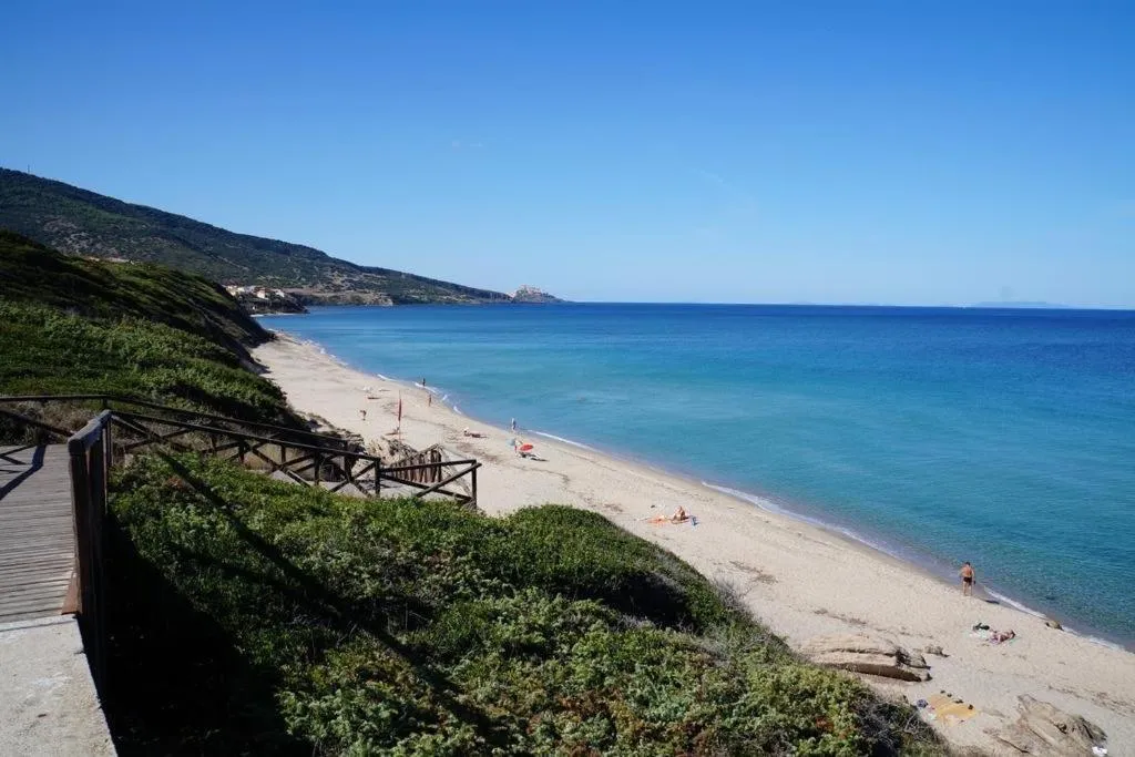 Spiaggia sabbiosa con mare azzurro, passerella in legno e colline verdi sulla costa