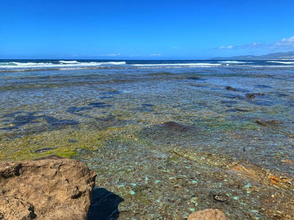Acqua di mare cristallina con fondale roccioso, onde e cielo azzurro limpido