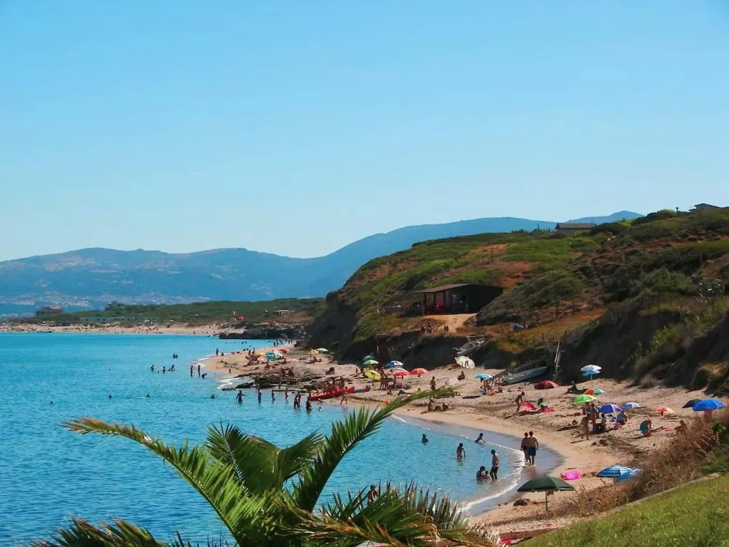 Spiaggia affollata con bagnanti, ombrelloni colorati, mare azzurro e colline sullo sfondo