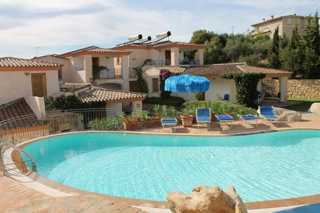 Piscina con acqua azzurra, ombrelloni e lettini davanti agli appartamenti