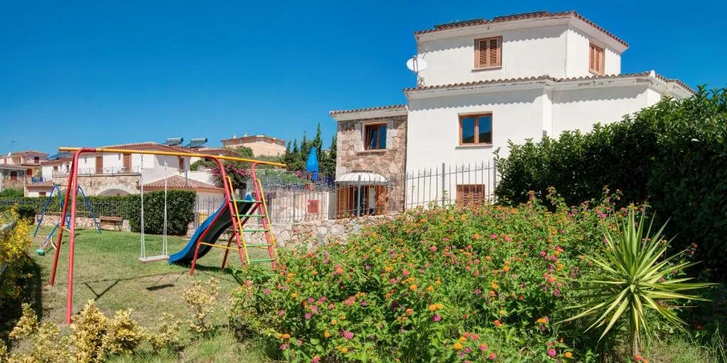 Area giochi per bambini con scivolo e altalena in un giardino fiorito accanto alla casa