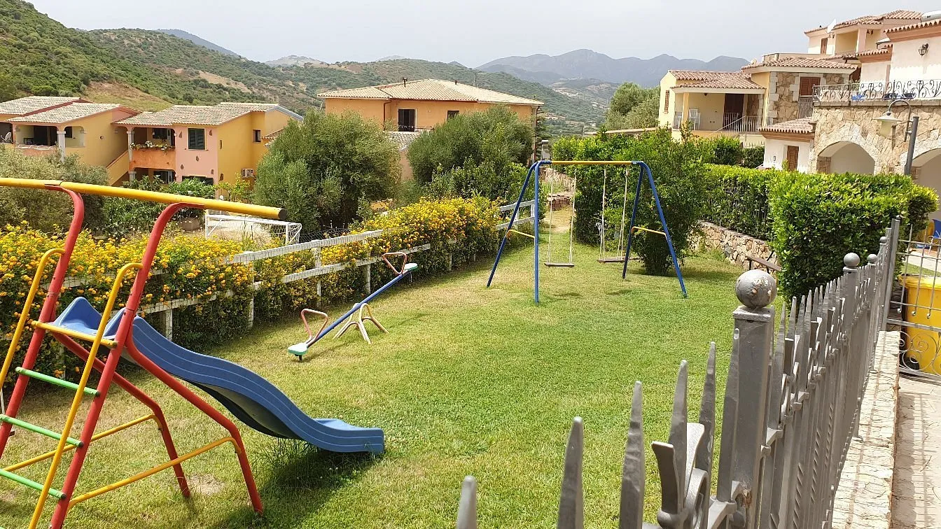 Parco giochi con scivolo e altalene su prato verde con vista sulle colline