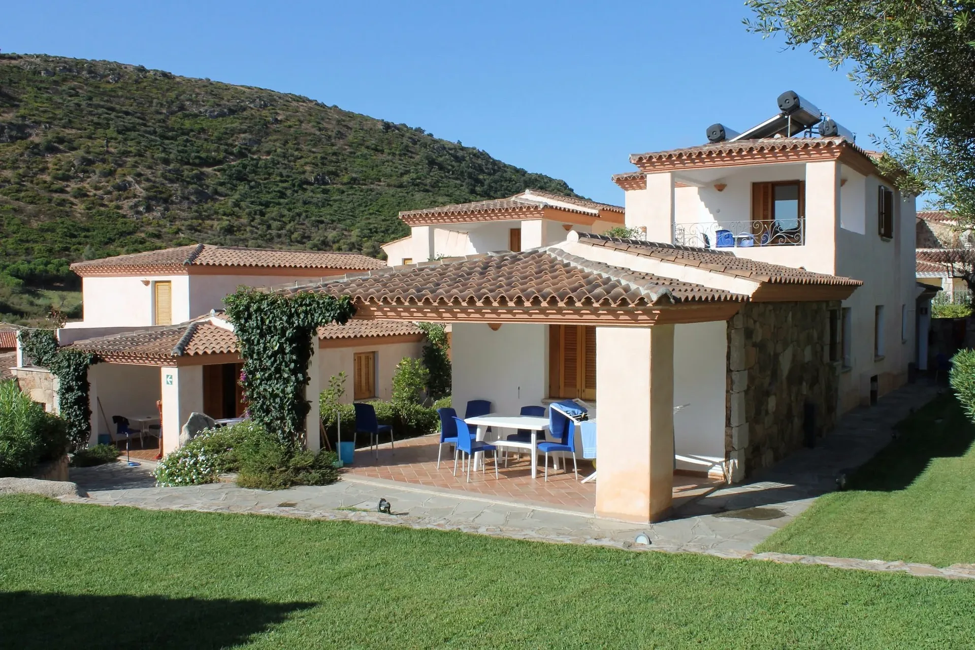 Veranda con tavolo e sedie blu davanti alla casa con tetto in tegole e giardino