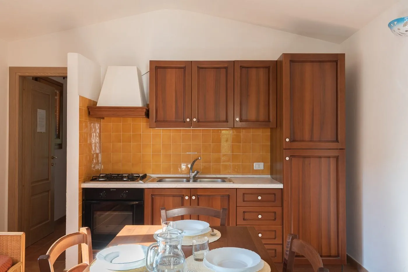 Cucina in legno con piastrelle gialle, fornelli e tavolo da pranzo apparecchiato