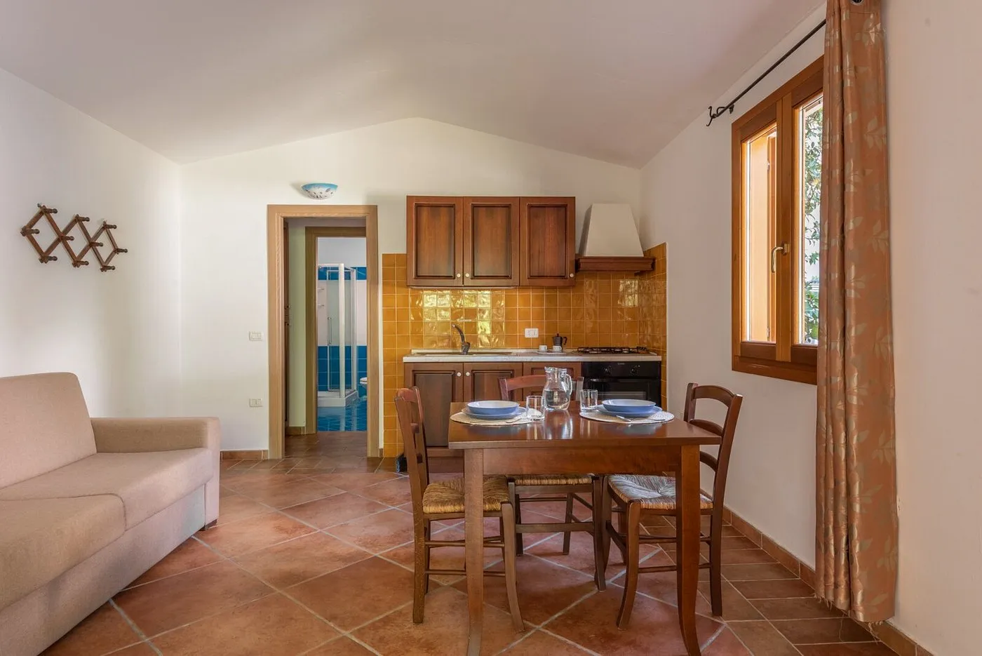 Soggiorno con divano, tavolo da pranzo in legno e angolo cottura con piastrelle gialle