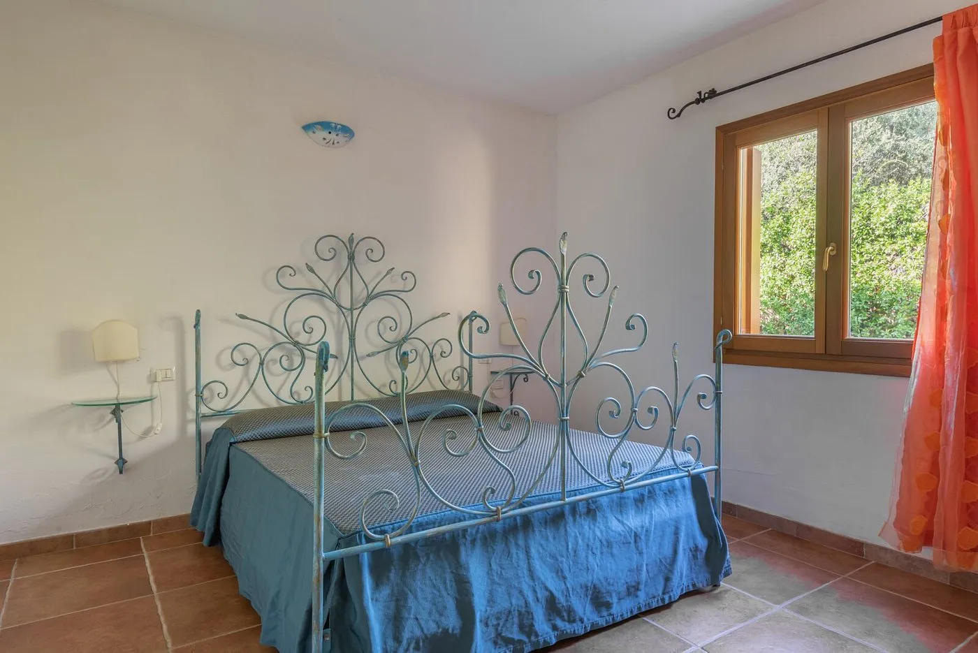 Camera da letto con letto matrimoniale in ferro battuto azzurro e finestra sul verde