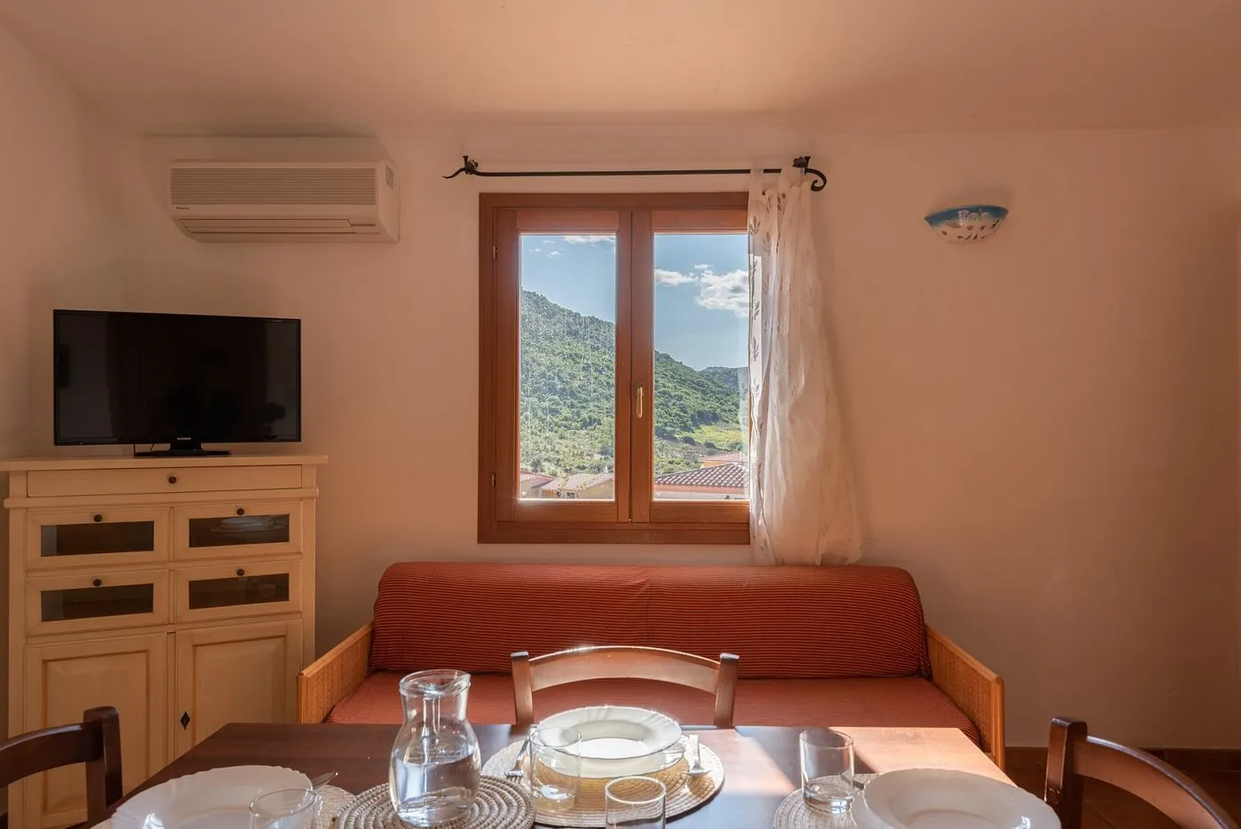 Soggiorno con divano, TV, tavolo apparecchiato e finestra con vista sulle colline