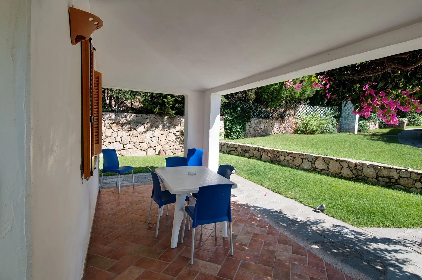 Veranda coperta con tavolo e sedie blu affacciata sul giardino con muretto in pietra