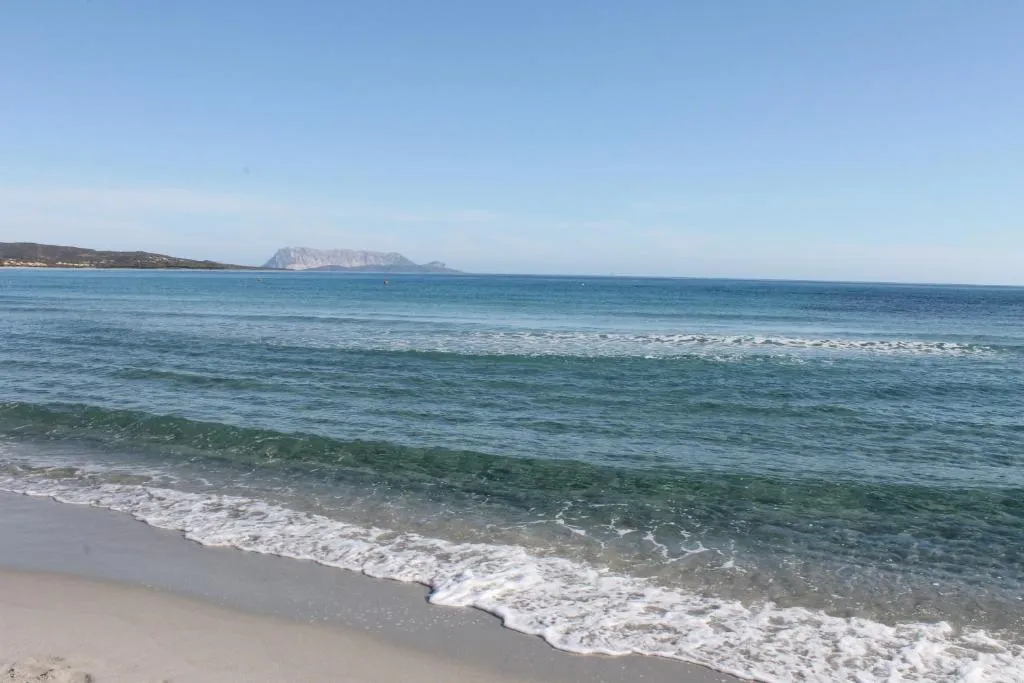 Spiaggia con mare blu, onde e l'isola di Tavolara all'orizzonte