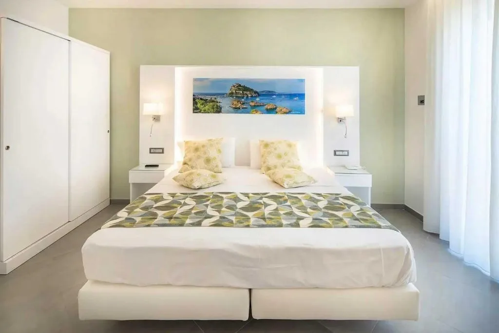 Camera moderna con letto matrimoniale bianco, testiera illuminata e tonalità verdi