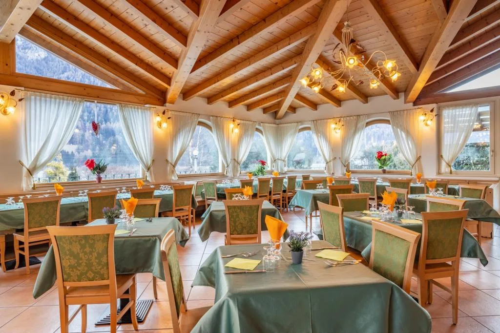 Ampia sala ristorante con soffitto in legno a vista, grandi finestre e tavoli apparecchiati