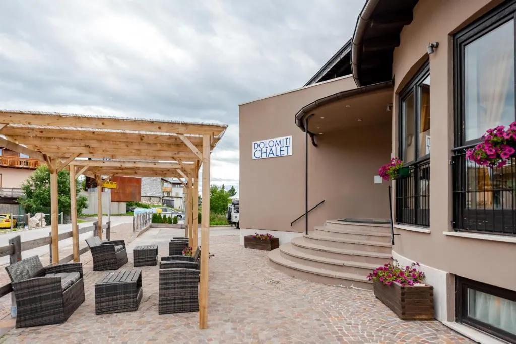 Ingresso dell'hotel Dolomiti Chalet con pergolato in legno, poltrone e fiori