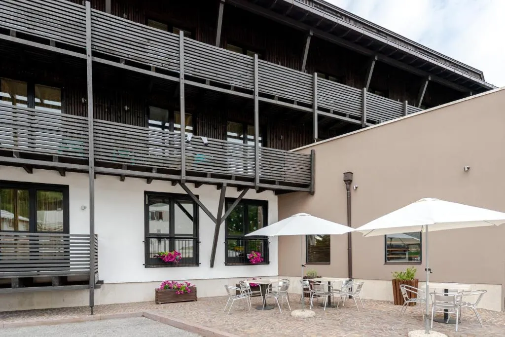 Cortile esterno dell'hotel con tavolini, ombrelloni bianchi e balconi in legno