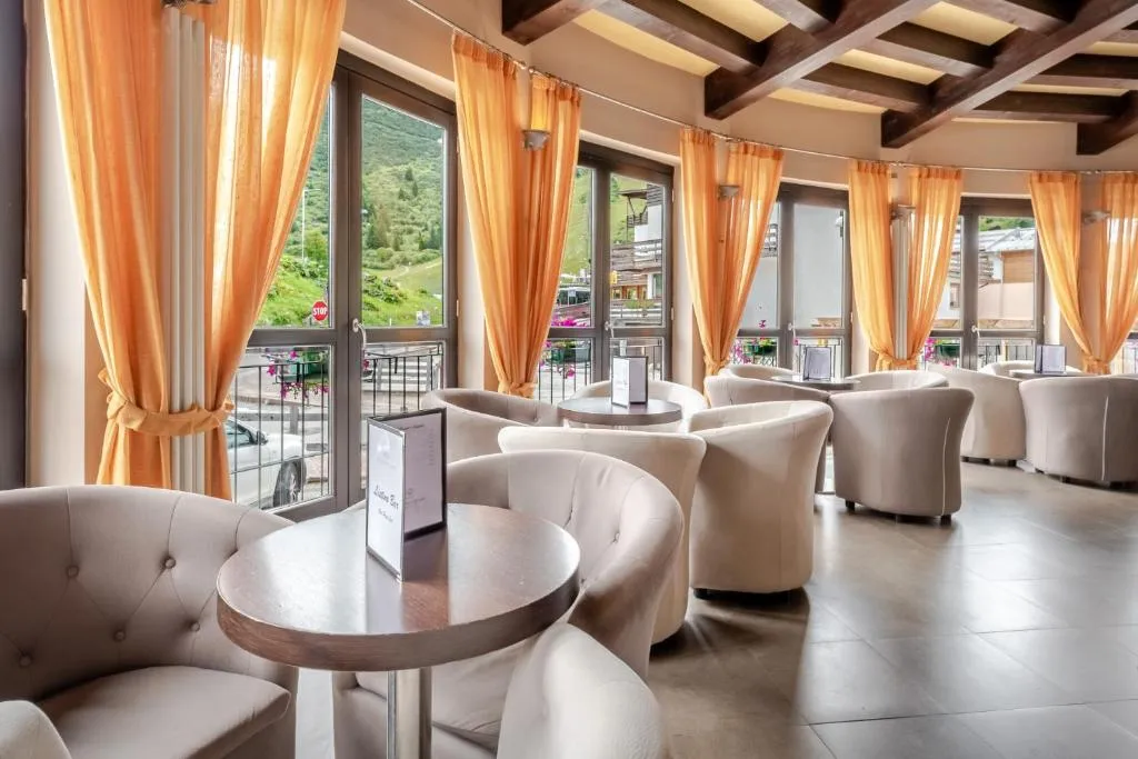 Sala lounge con poltrone bianche, tavolini rotondi e ampie vetrate con vista sulle montagne