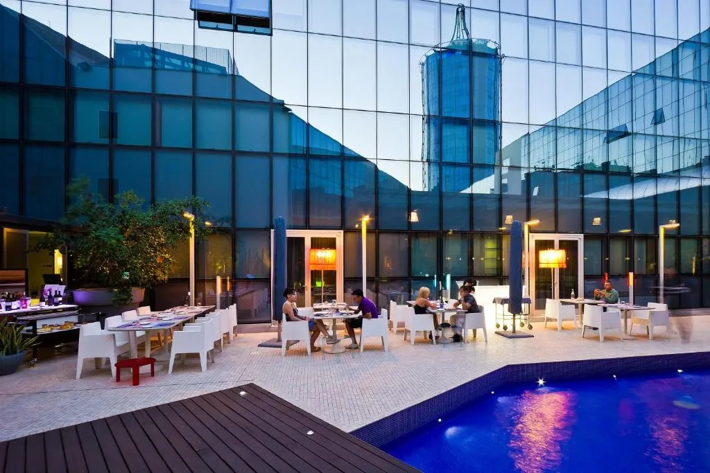 Terrazza esterna con piscina e tavoli serviti davanti a facciata a specchio