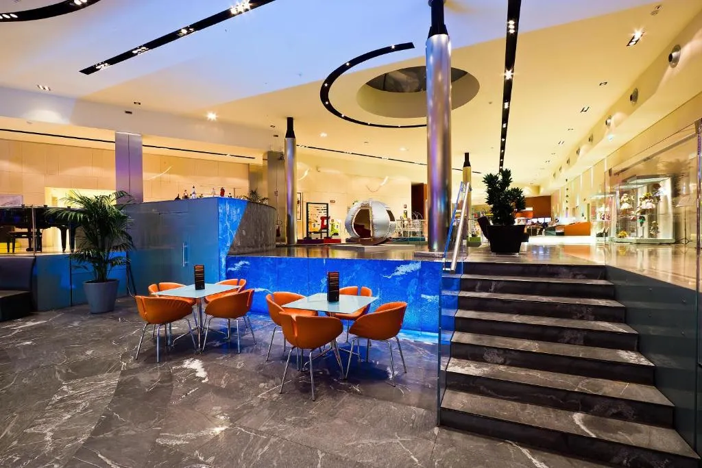 Hall moderna con tavoli arancioni, scalinata in marmo e parete in vetro blu