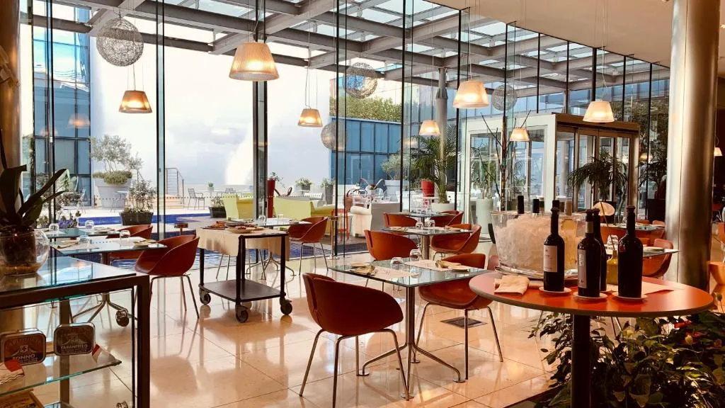 Sala ristorante luminosa con tavoli, sedie arancioni e ampie vetrate