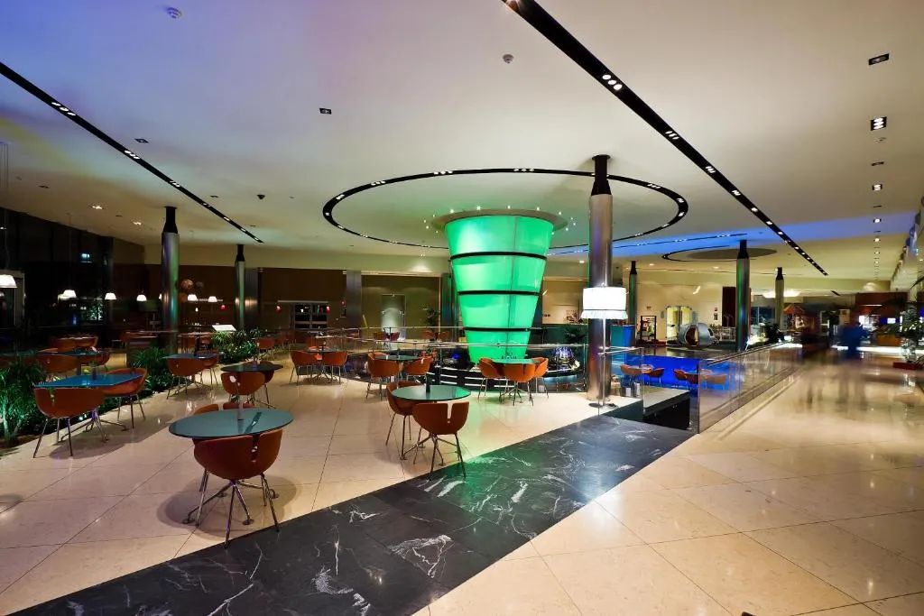 Ampia hall lounge con tavoli, sedie e colonna luminosa verde centrale