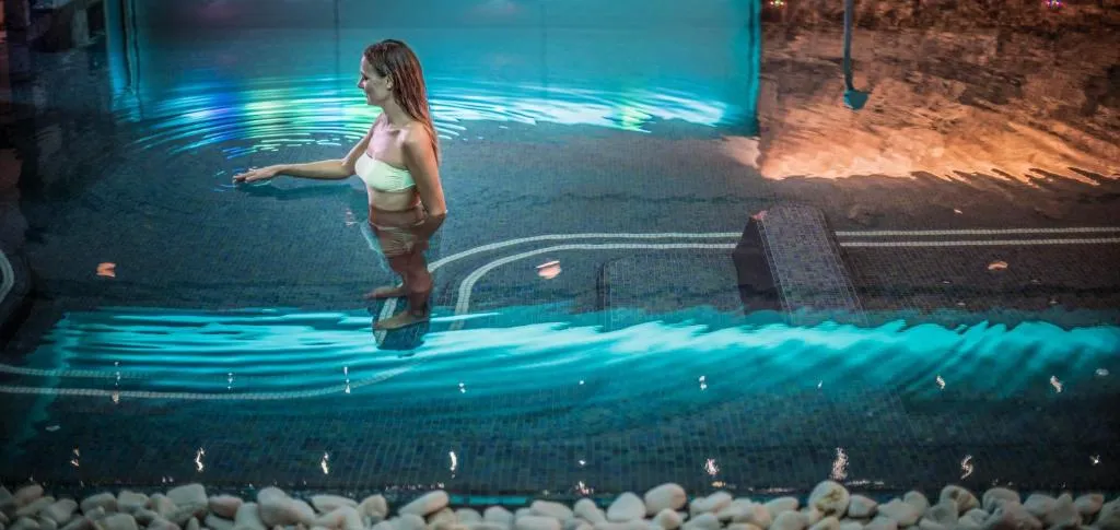 Donna in piscina interna con illuminazione blu e bordo di ciottoli bianchi