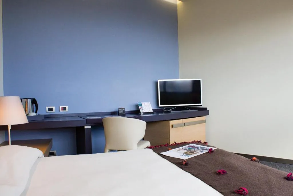 Camera con letto, scrivania, TV e parete azzurra