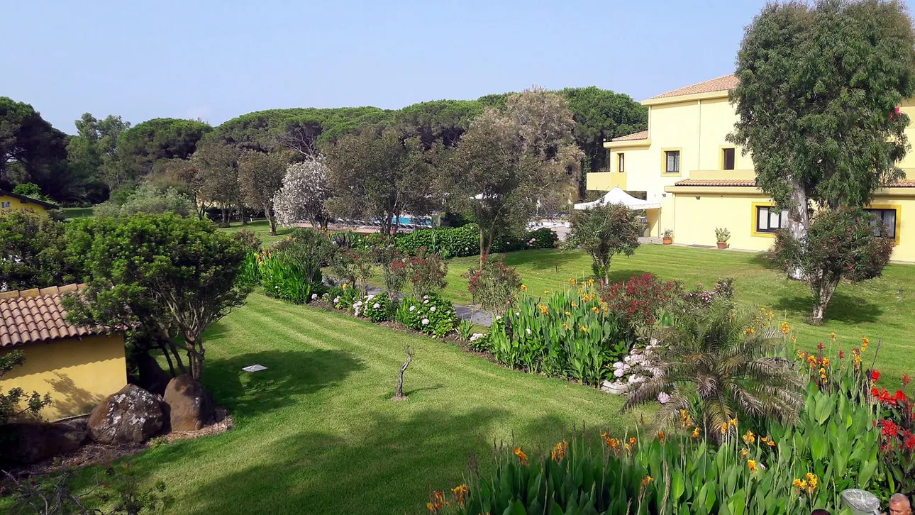 Ampio giardino verde con aiuole fiorite e edificio giallo del resort