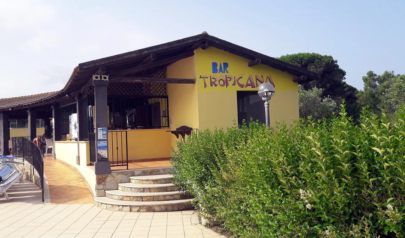 Bar Tropicana con edificio giallo, scalinata in pietra e siepe verde